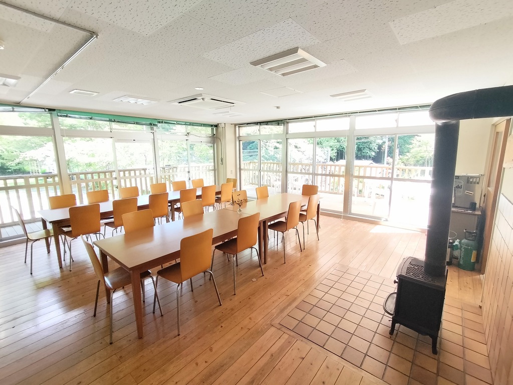 Shared dining hall with tables and a wood-burning stove at Shimonanosato