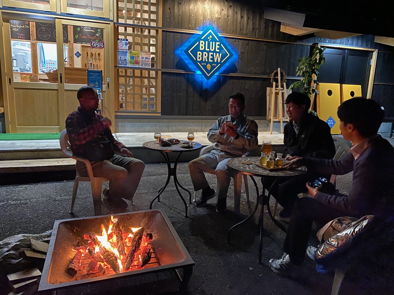 Guests gathered around a fire pit outside Blue Brew at night.
